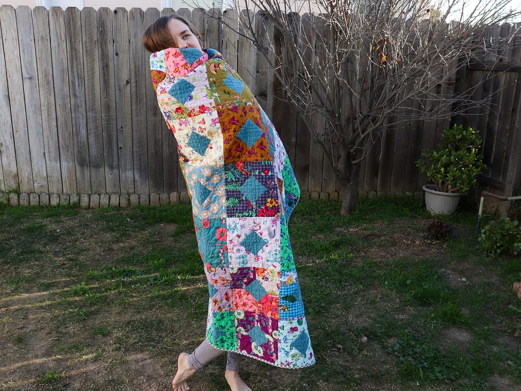 Miranda wrapped in her completed pandemic quilt.
